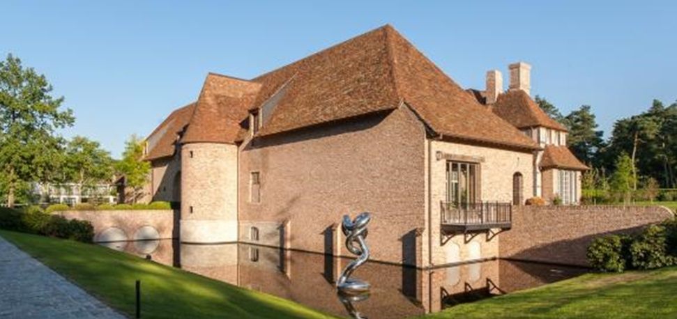 Kasteelhoeve met nieuw gevoegde gevel in rode baksteen, weerspiegeld in de slotgracht